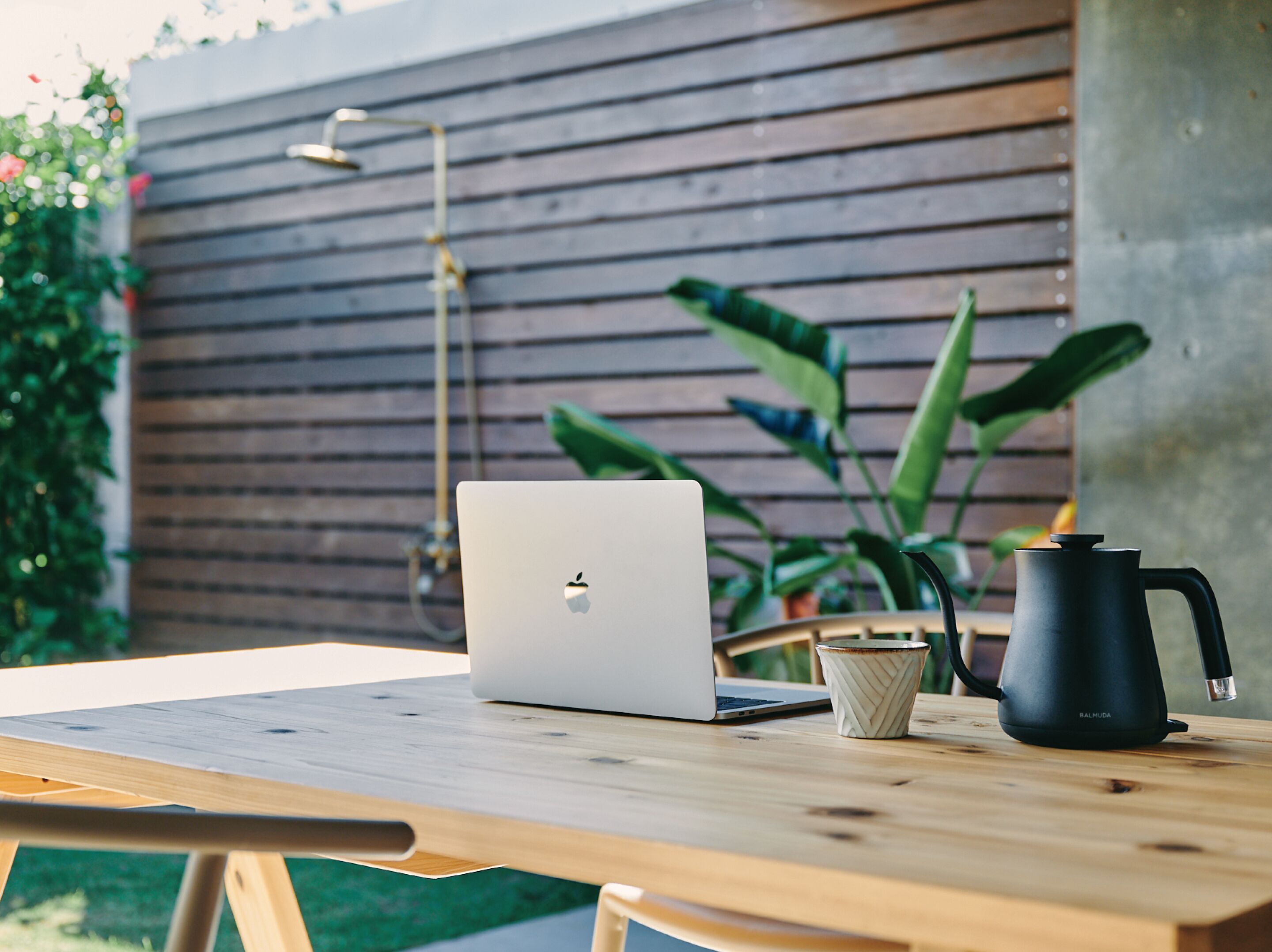 Een houten tafel met een laptop, een beker en een zwarte koffiezetapparaat.