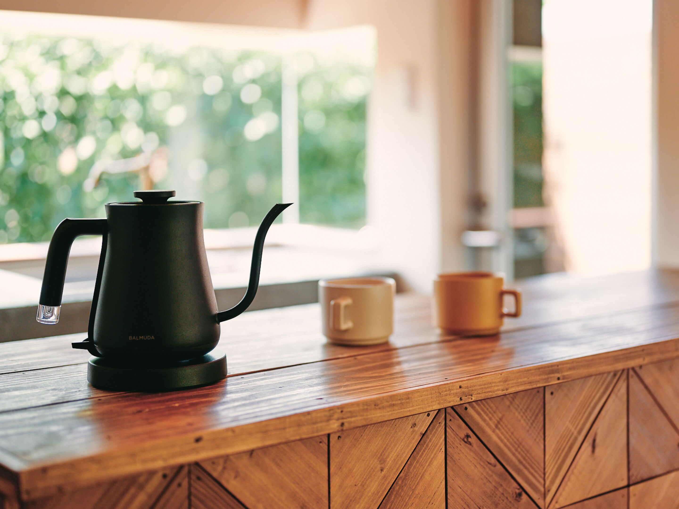 A wooden table with a black kettle and two yellow mugs.
