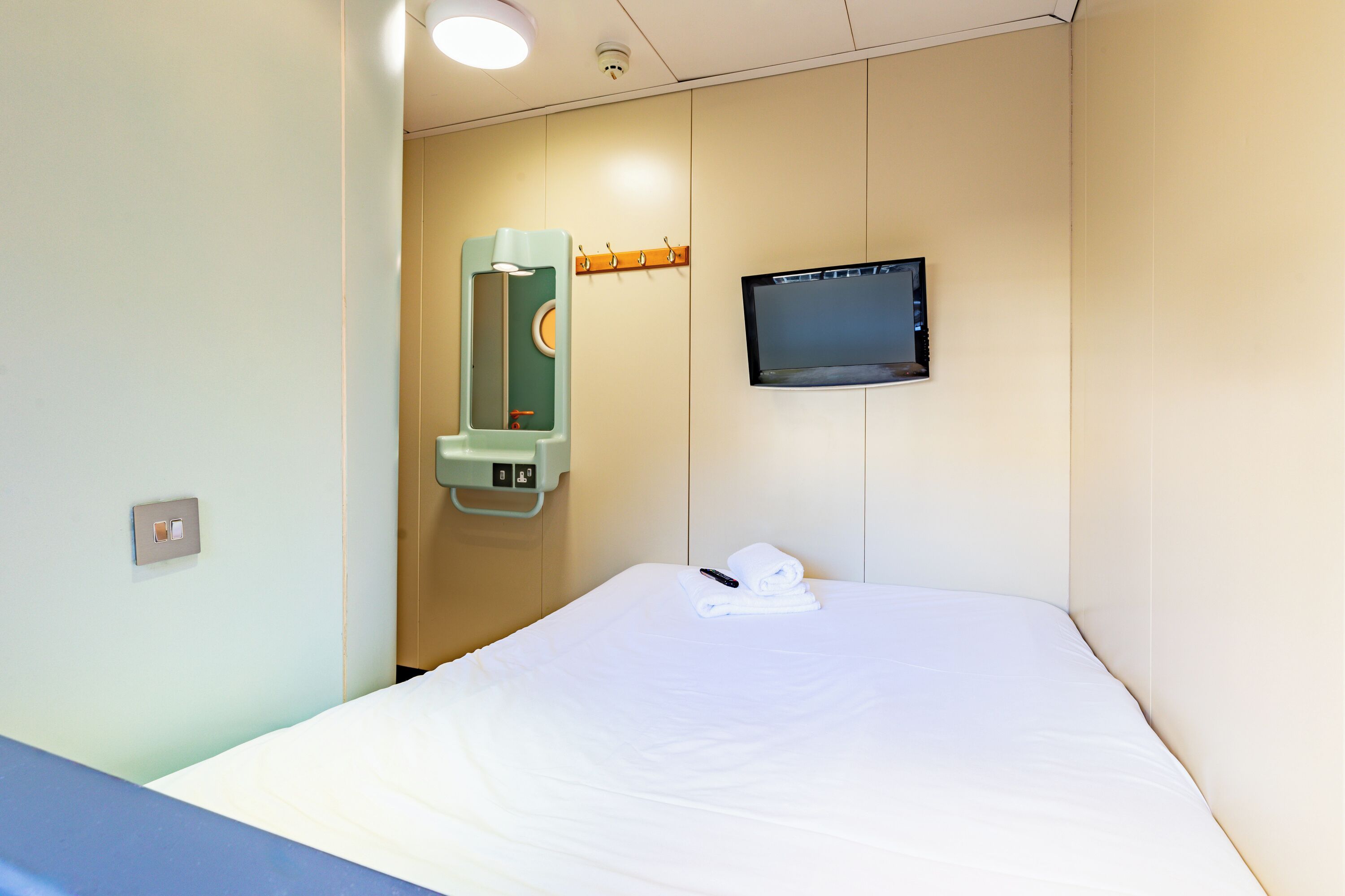 A hotel room with a bed, a television mounted on the wall, and a mirror with a towel on it.