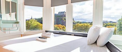 A hotel room with a large bed, a TV, and a view of a castle through the windows.