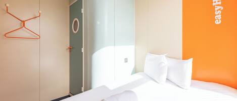 Una habitación de hotel con cama, una toalla blanca, perchero y armario.
