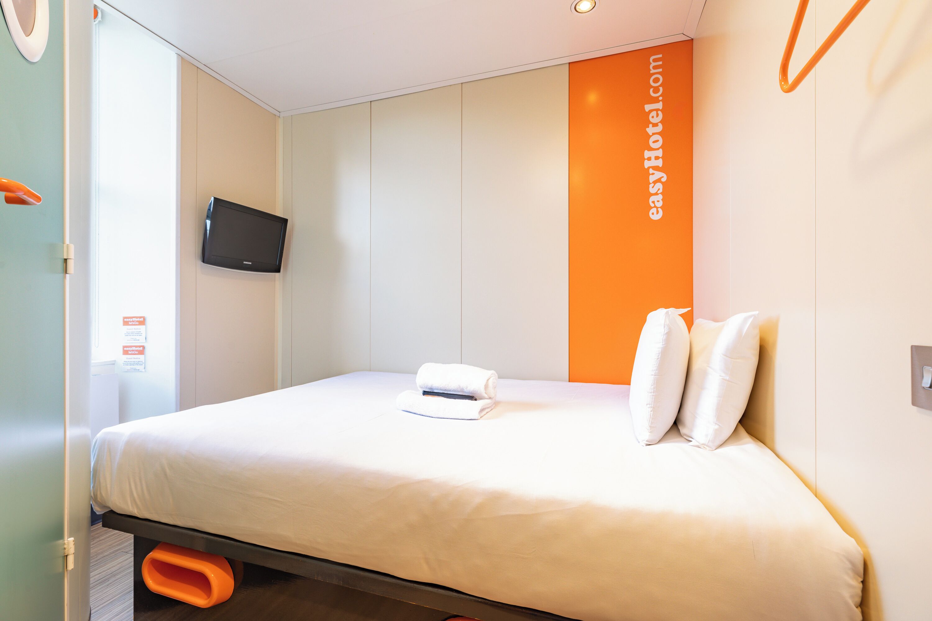 A hotel room with a bed, a flat-screen TV mounted on the wall, and a sign with the hotel's name.