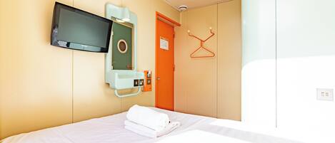 A hotel room with a bed, a television mounted on the wall, an orange door, and a coat rack.