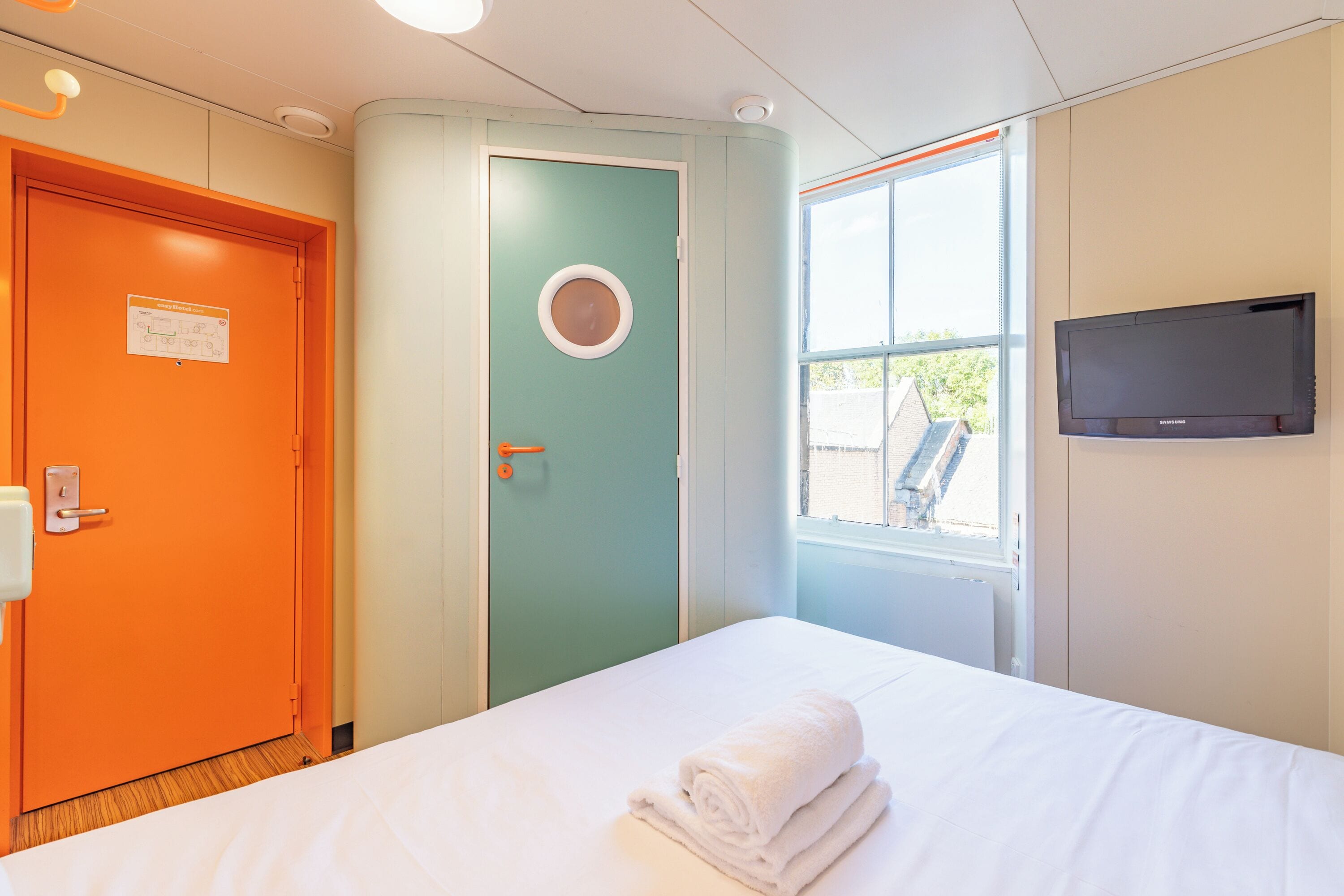 Une chambre d’hôtel avec un lit, une télévision, une fenêtre et une porte orange.