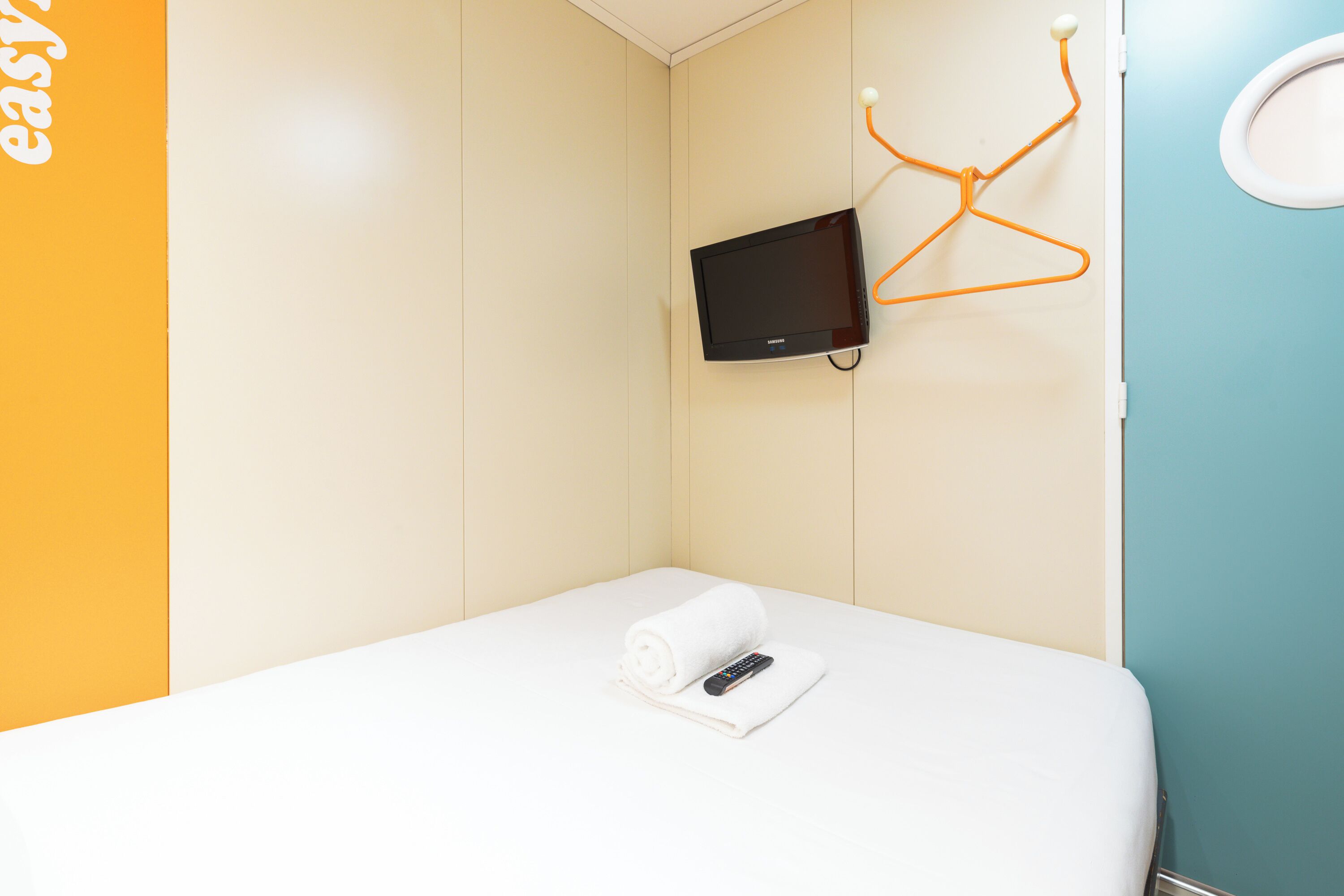 A hotel room with a bed, a TV mounted on the wall, and a towel on the bed.
