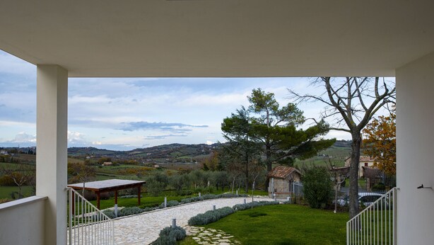 Uma varanda com um caminho de pedra que leva a uma área gramada, com um pérgola e vista para o campo.