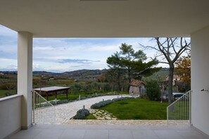 Un balcón con un camino de piedra que lleva a una zona ajardinada con un pérgola y vistas al campo.