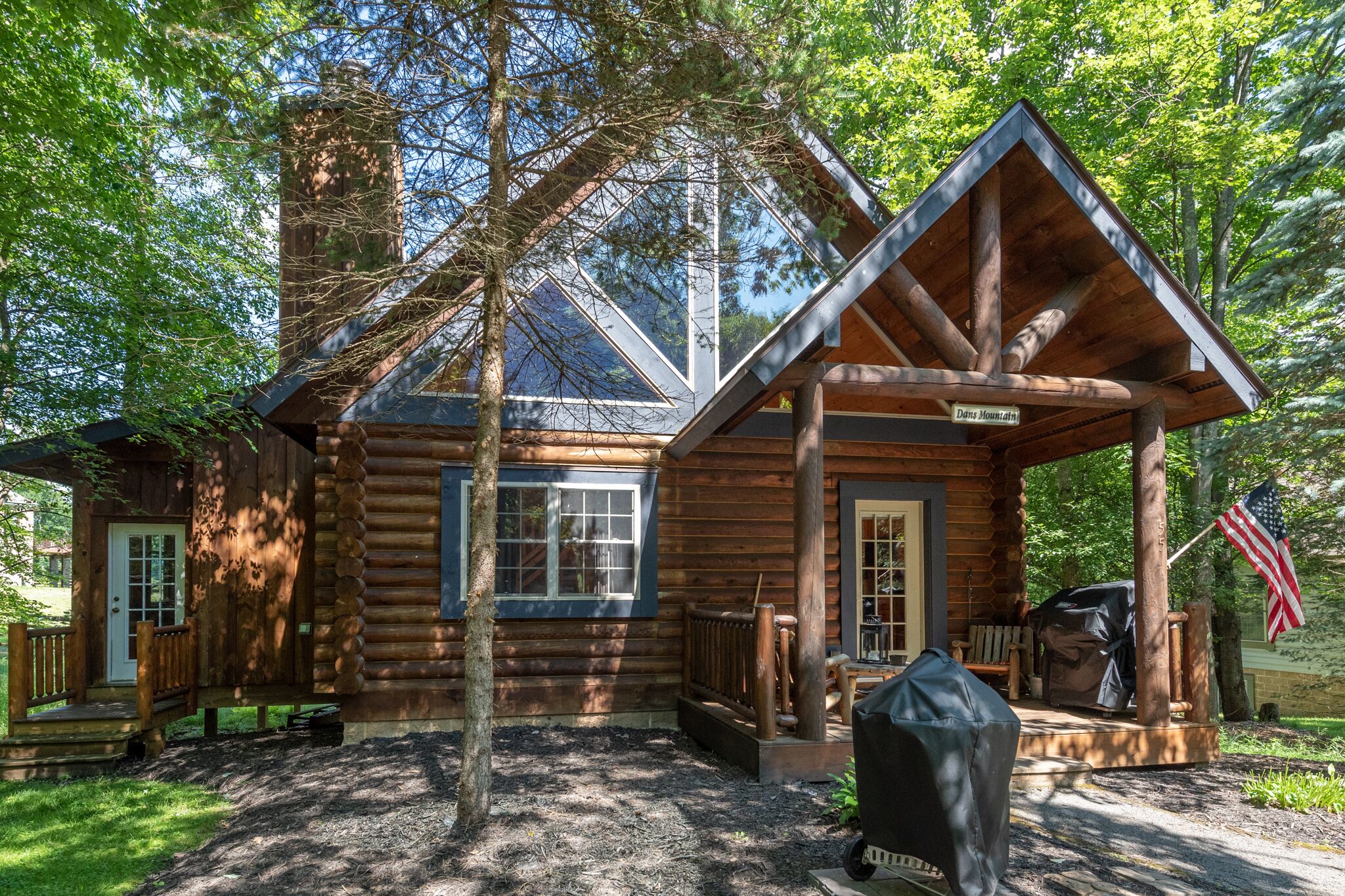 A rustic log cabin with a porch, a chimney, and an American flag.