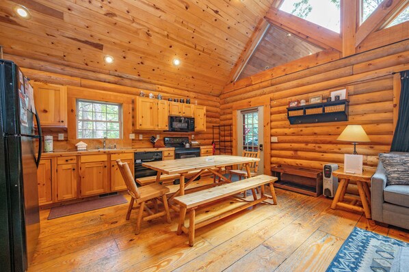 A log cabin with a wooden interior, including a kitchen with a microwave, a dining table with benches, and a sofa. - Cozy Dog Friendly Log Cabin w/ Hot Tub & Fireplace (Oakland)