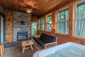 Ein gemütliches Blockhaus-Interieur mit Kamin aus Stein, Holzmöbeln und großen Fenstern mit Blick auf den Wald.