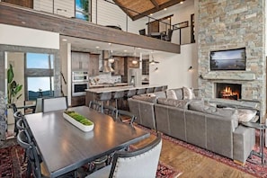 A modern kitchen with a stone fireplace, a dining area with a large table, and a cozy seating area with a sofa. - Exceptional Waterfront Luxury Home | Hot Tub (Sandpoint)