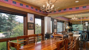 A dining area with a large wooden table and chairs, decorated with American flags, and large windows offering a view of trees and buildings.