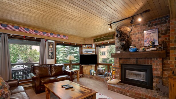 A cozy living room with leather furniture, a fireplace, and a large window overlooking greenery.
