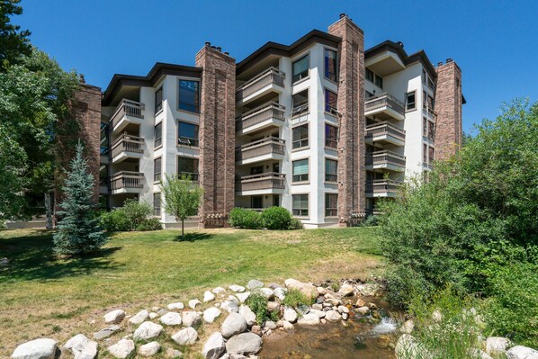 Un immeuble à plusieurs étages doté de balcons, d’une zone herbeuse et d’un petit ruisseau.