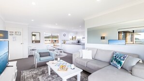 Ein modernes Wohnzimmer mit grauem Sofa, einem Couchtisch und einem Essbereich mit weißen Stühlen.