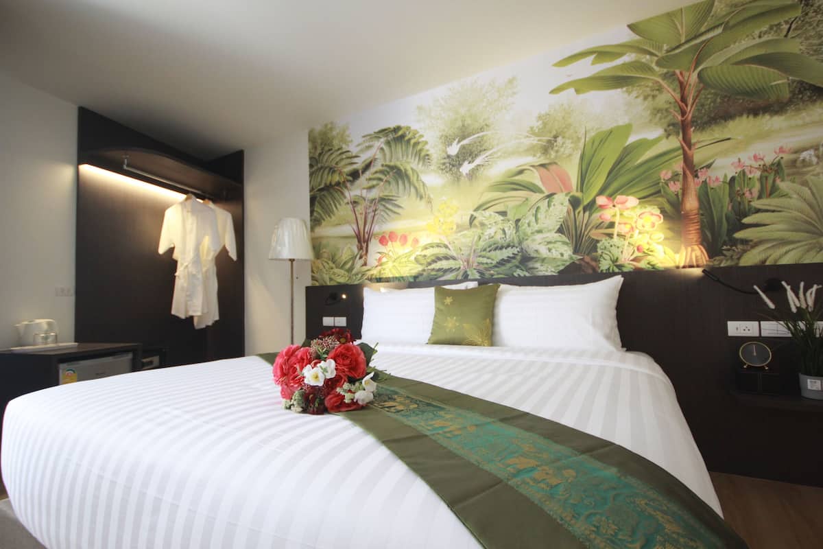 Une chambre d’hôtel avec un grand lit, une table de chevet, une lampe, une fresque murale et un bouquet de fleurs.