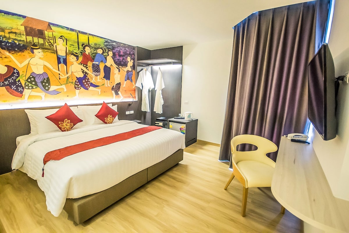 Une chambre d’hôtel avec un grand lit, un bureau, une chaise, une télévision et une fresque colorée sur le mur.
