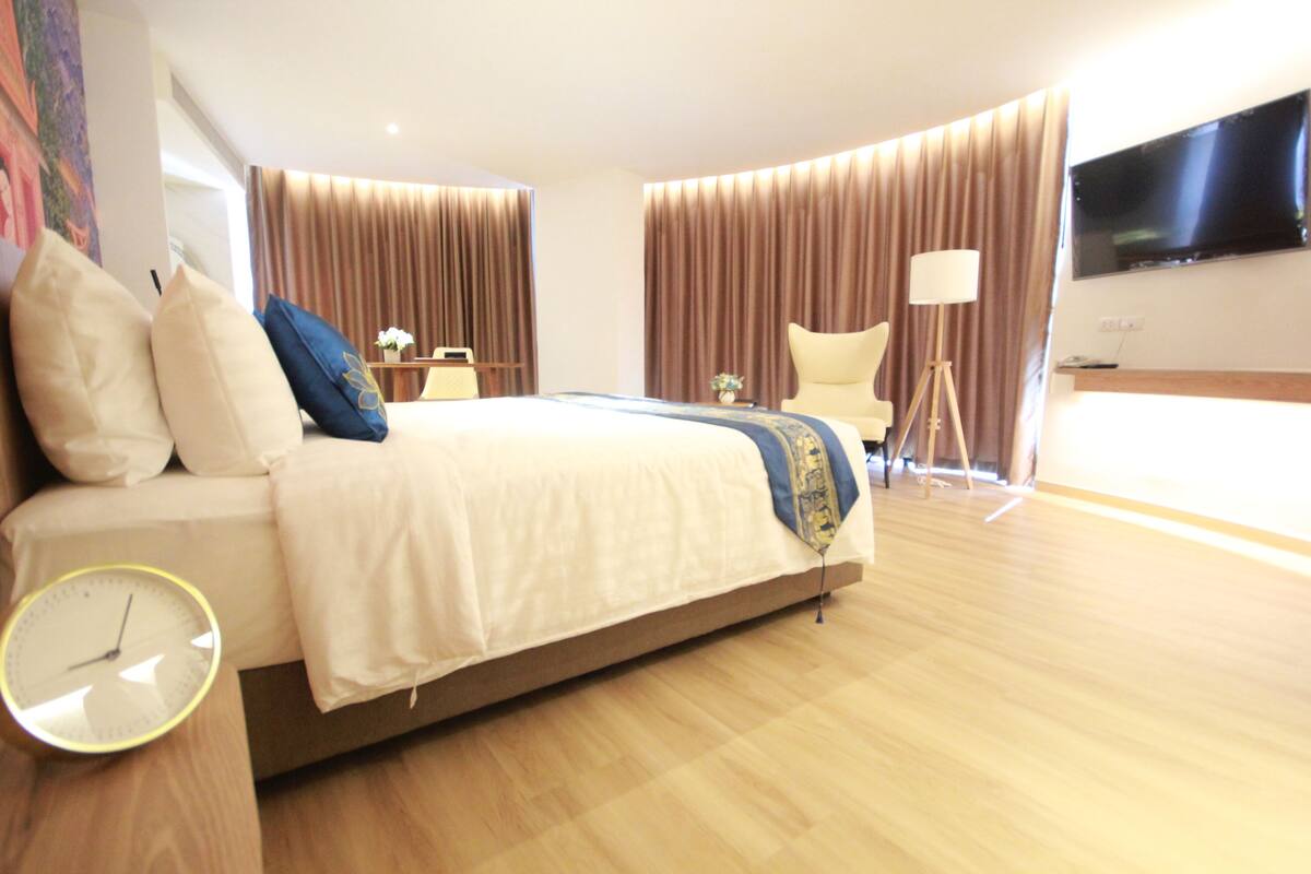 Une chambre d’hôtel moderne avec un grand lit, une table de chevet, une lampe, un téléviseur et une horloge.