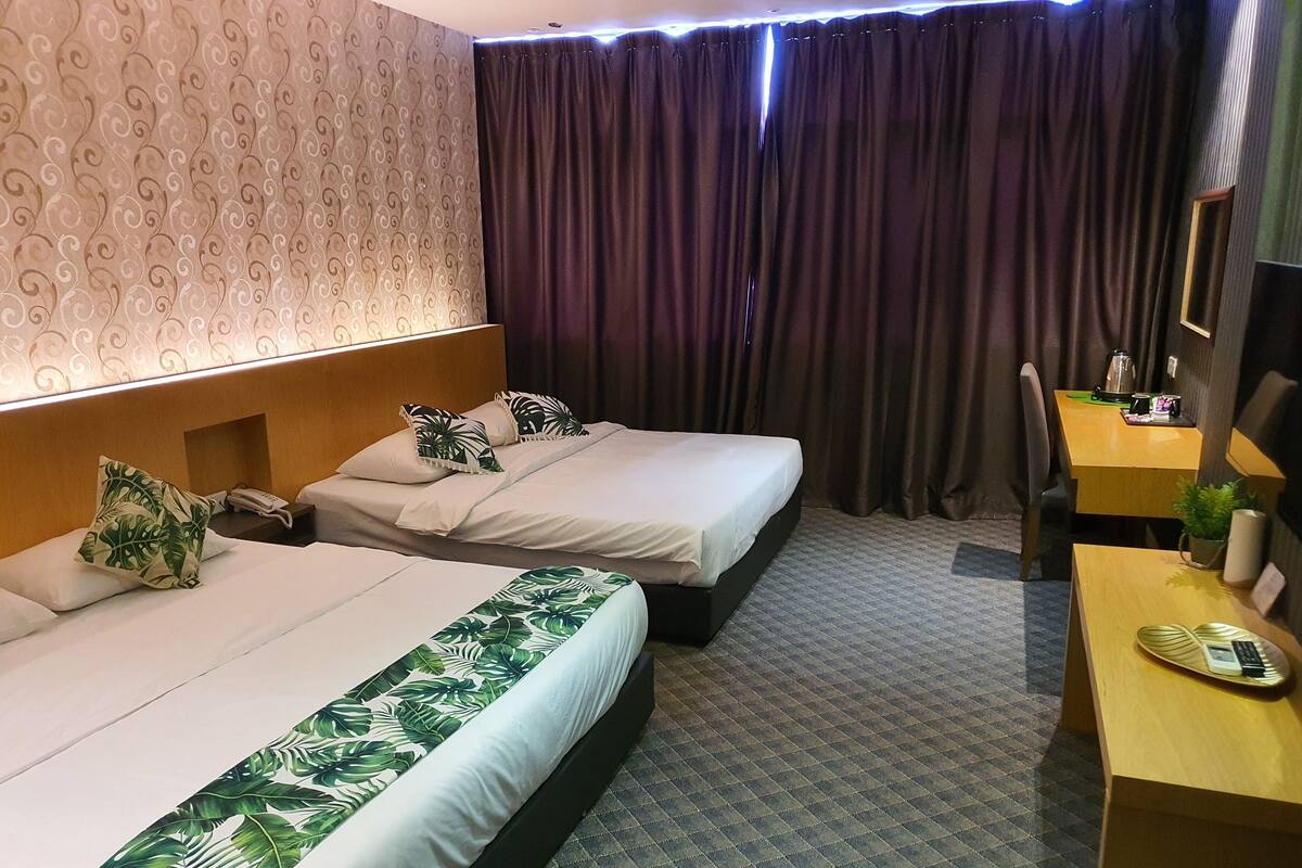Habitación de hotel con dos camas, un escritorio, una silla, un teléfono, una cafetera y una planta.