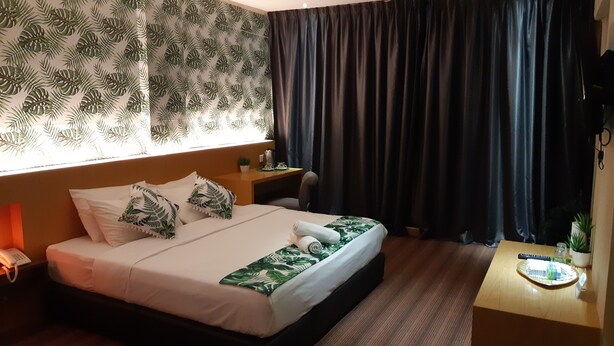 A hotel room with a bed, a small desk, a telephone, and a window with curtains. - Grandeur Hotel and Spa (Malacca City)