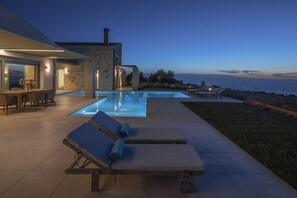 A modern house with a swimming pool, outdoor seating, and a view of the sea.