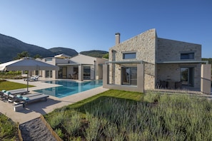 A modern house with a swimming pool, stone exterior, and a well-maintained lawn.