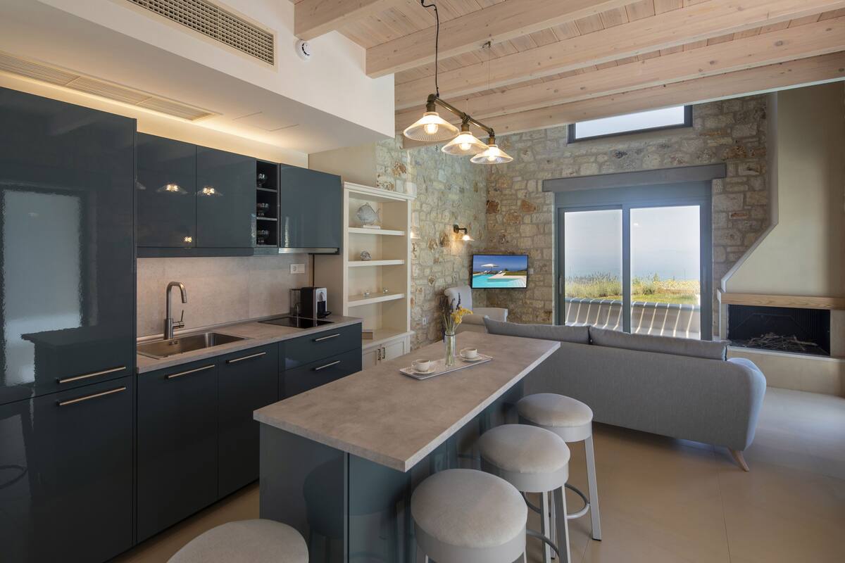 A modern kitchen with dark cabinets, a large island with stools, a stone accent wall, and a television.