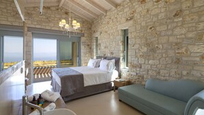 Een slaapkamer met een stenen muur, een bed, een bank, een kroonluchter en uitzicht op het landschap.