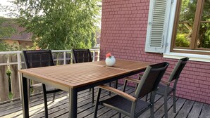 A wooden deck with a table and chairs, a brick wall, and a window with shutters. - Welcome to our vacation home Martini! (Waldachtal)