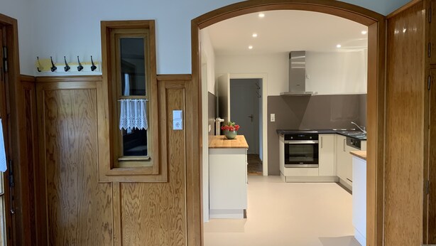A modern kitchen with wooden cabinetry, a built-in oven, and a countertop with a vase of flowers. - Welcome to our vacation home Martini! (Waldachtal)