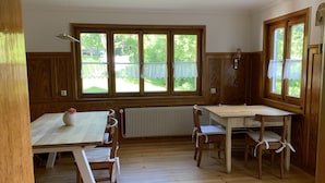 A room with wooden paneling, a radiator, a table with chairs, and large windows with curtains. - Welcome to our vacation home Martini! (Waldachtal)