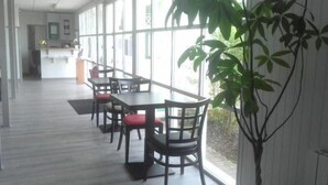 A dining area with tables and chairs, large windows, and a potted plant. - Premiere Classe Rennes Ouest - Le Rheu (Le Rheu)