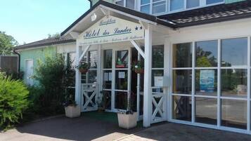 Un hotel llamado "Hotel des Landes" con una entrada acogedora, ventanas amplias y plantas en macetas.