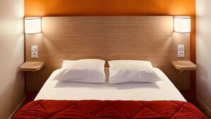 A hotel room with a bed, two bedside lamps, and a red quilted bedspread. - Premiere Classe Rennes Ouest - Le Rheu (Le Rheu)