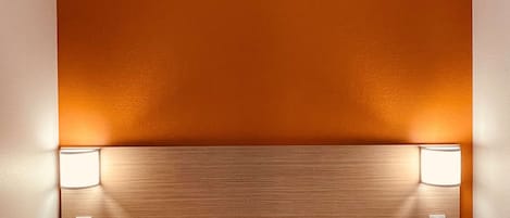 Een hotelkamer met een bed, twee bedlampen en een rode geborduurde sprei.