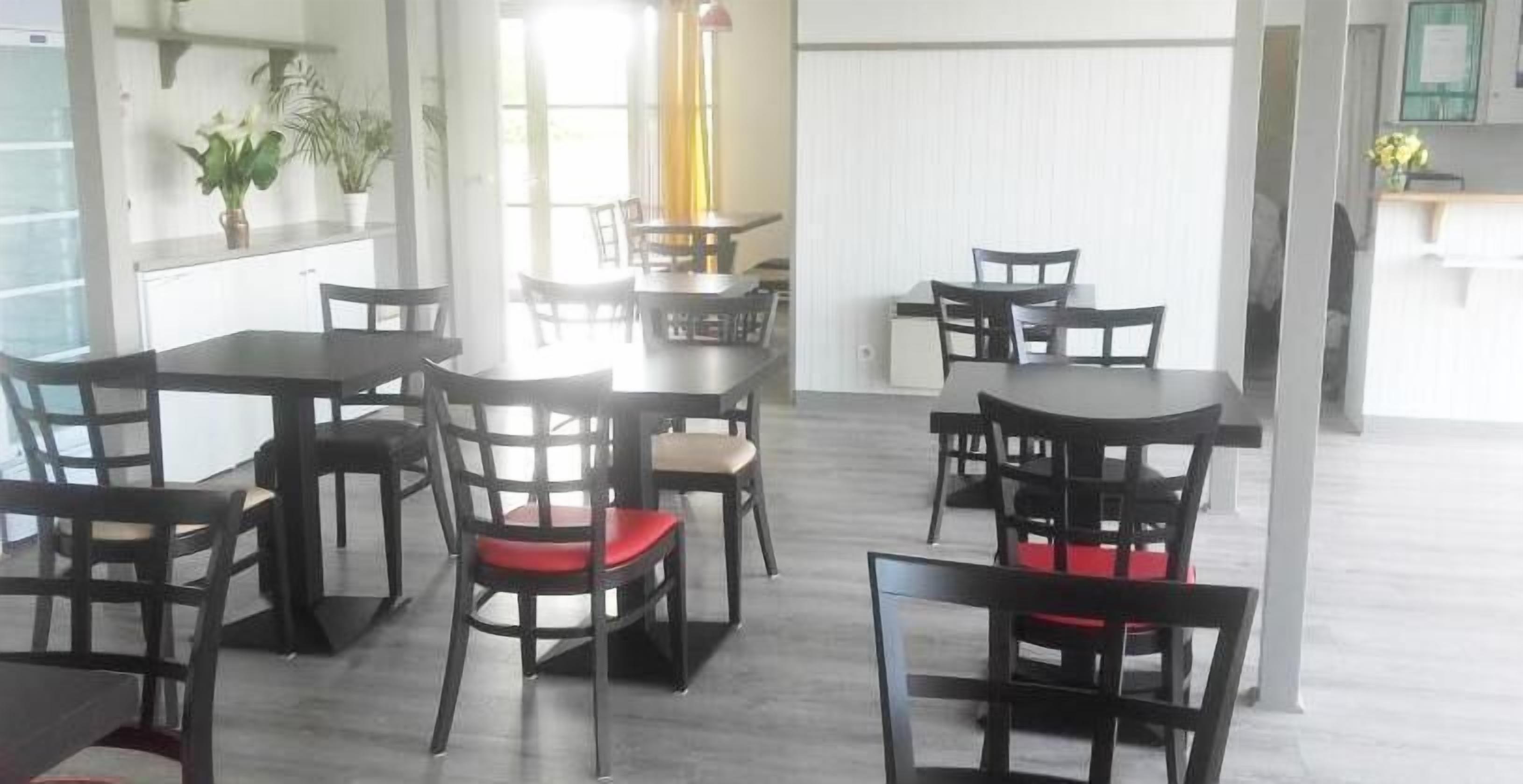 A dining area with multiple tables and chairs, some with red cushions.