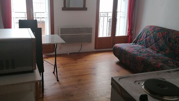 Une petite pièce agréable, dotée d’un plancher en bois, d’une table à manger avec des chaises, d’un canapé et d’une kitchenette équipée d’une cuisinière.