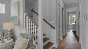 Et moderne interiør med en trappe, der fører til en anden etage, et spiseområde med bord og stole, og et køkken, der kan ses gennem en åben dør.