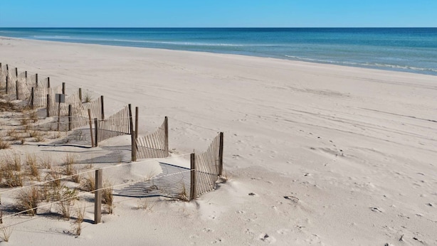 En sandstrand med et træhegn og et skilt.