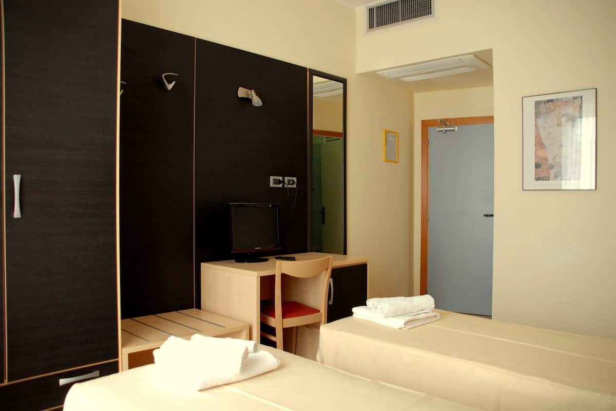 Hotellihuone, jossa on kaksi sänkyä, työpöytä, jossa on televisio, vaatekaappi ja kylpyhuoneen ovi.