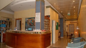 A reception area with a curved counter, a sign reading "ARNO", and a wall-mounted menu board.