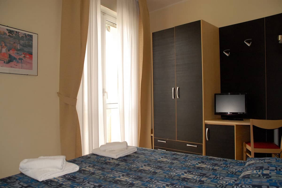 Hotellihuone, jossa on sänky, vaatekaappi, televisio ja tuoli.