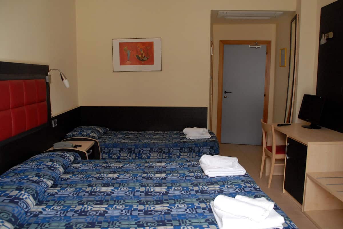 Hotellihuone, jossa on kaksi sänkyä, työpöytä, tuoli, televisio ja ovi.