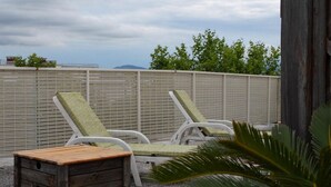 A rooftop terrace with two white lounge chairs and a wooden bench.