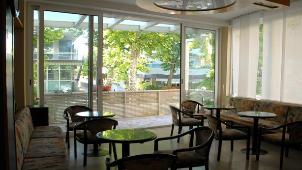 A modern indoor seating area with a sofa, chairs, and tables, large windows with a view of greenery and buildings outside.