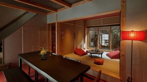 Ein traditioneller japanischer Raum mit Tatami-Bodenbelag, einem niedrigen Holztisch und Blick ins Freie durch ein großes Fenster.