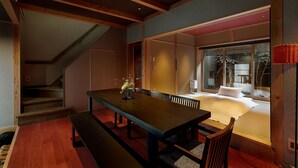 Ein modernes Interieur mit einem Holztisch, einer Sitzbank und Blick auf einen traditionellen japanischen Raum durch eine Glastür.