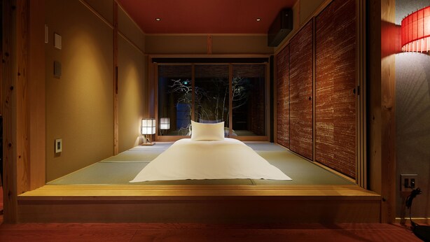 Ein traditioneller japanischer Raum mit Tatami-Böden, einer niedrigen Plattform-Liege, Schiebetüren und Blick ins Freie.
