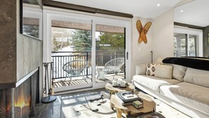 A modern living room with a fireplace, a sofa, a coffee table, and a balcony with outdoor furniture. - Remodeled Aspen Gem! 1 Block to Aspen Mtn, Balcony with Views, W/D, Parking & Walk to Town (Aspen)