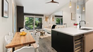 A modern kitchen with a central island, a dining area with a wooden table and white chairs, and a living area with a sofa and decorative wall art. - Remodeled Aspen Gem! 1 Block to Aspen Mtn, Balcony with Views, W/D, Parking & Walk to Town (Aspen)